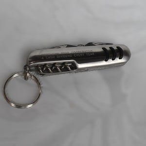 May include: A silver multi-tool keychain with a keyring. The tool has several functions and the text "NORTHERN STAR COOPERATIVE A CASH DIVIDEND EVERY YEAR" is printed on the side. The tool is on a white background.