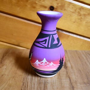 May include: Purple ceramic vase with a black and white geometric design and a painted scene of mountains and trees.