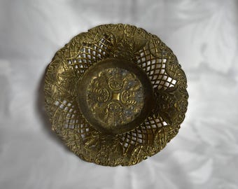 Könnte beinhalten: Eine goldfarbene, dekorative Schale aus Metall mit einem komplizierten Design. Die Schale hat eine runde Form und einen erhöhten Rand. Das Design zeigt ein sich wiederholendes Muster aus Blättern und Blumen.