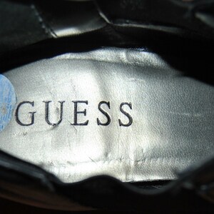 May include: Close-up of the inside of a black shoe with a silver insole that says "GUESS" in black lettering.