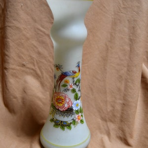 May include: A white frosted glass vase with a yellow rim and a floral design featuring a peacock, flowers, and leaves. The vase has a bulbous base and a narrow neck.