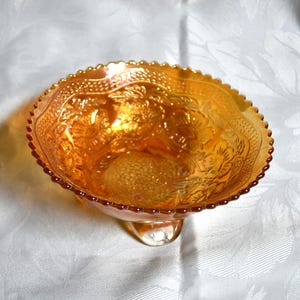 May include: A vintage amber glass candy dish with a footed base and an intricate floral design.