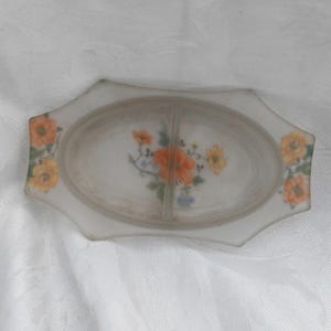 May include: A vintage divided dish with a floral design. The dish is white with an oval center and a decorative edge. Orange and yellow flowers are painted on the dish.