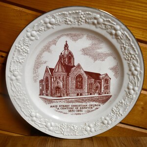 May include: White decorative plate featuring a maroon church illustration. The plate has a gold rim and a white embossed floral border. Text on the plate reads "Main Street Christian Church, A Century of Service, 1851-1951."