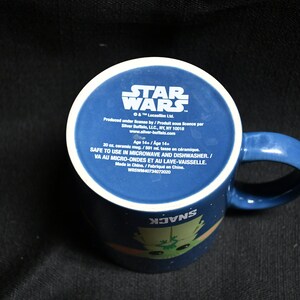 May include: A blue ceramic mug with a white rim and handle. The mug features a Star Wars logo and a cartoon image of a character from the movie. The text on the mug reads "Star Wars", "Safe to use in microwave and dishwasher", and "Made in China".