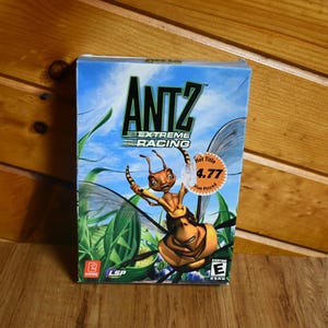 May include: A video game box for "Antz Extreme Racing" features a cartoon ant character with a blue sky and green foliage background. The box has a "Hot Title" sticker with a price of 4.77. The game is rated "Everyone" by the ESRB.