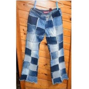 Peut inclure: Pantalon en jean bleu patchwork suspendu sur un fond en bois. Le pantalon présente un motif en damier de différentes nuances de denim bleu. Il est suspendu à un cintre blanc.