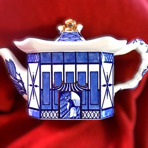 May include: A blue and white porcelain teapot with a gold lid and handle. The teapot is decorated with a geometric pattern and a scene of a person in a building.