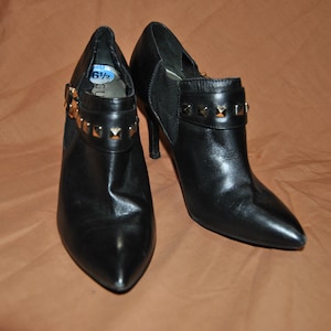 May include: Black leather ankle boots with gold-toned studs and a pointed toe. The boots have a high heel and a zipper on the side. The size tag says "6 1/2".