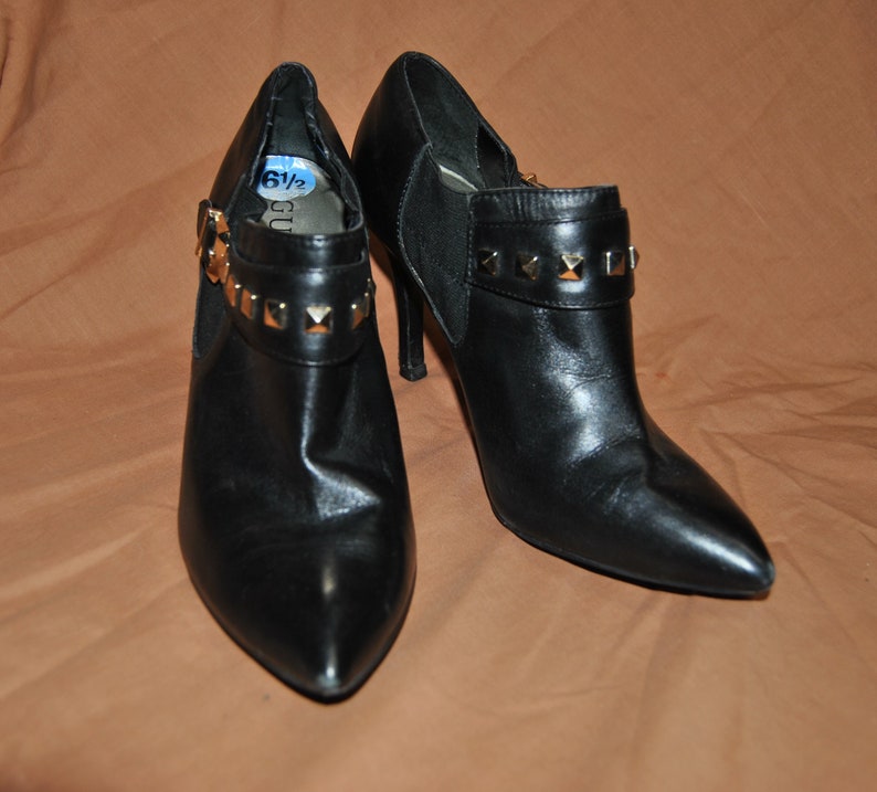 May include: Black leather ankle boots with gold-toned studs and a pointed toe. The boots have a high heel and a zipper on the side. The size tag says "6 1/2".