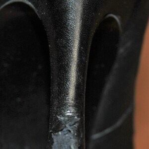 May include: Close-up of the bottom of a black leather heeled shoe. The heel is worn and has a small tear in the leather.