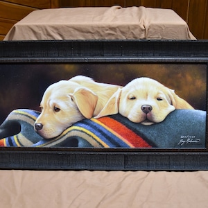 May include: Framed painting of two yellow Labrador Retriever puppies sleeping on a colorful blanket. The painting is signed by the artist, "Jay Johnson".