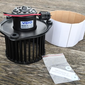 Puede incluir: Un motor de soplador automotriz VDO PM3340 12V negro con una carcasa negra y aspas de ventilador. Incluye una caja de cartón blanca y una pequeña bolsa de plástico con dos espaciadores blancos. El motor tiene cables rojos y negros.