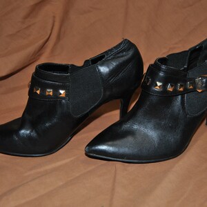May include: A pair of black leather ankle boots with gold-toned studs and a pointed toe. The boots have a high heel and a back zipper closure.