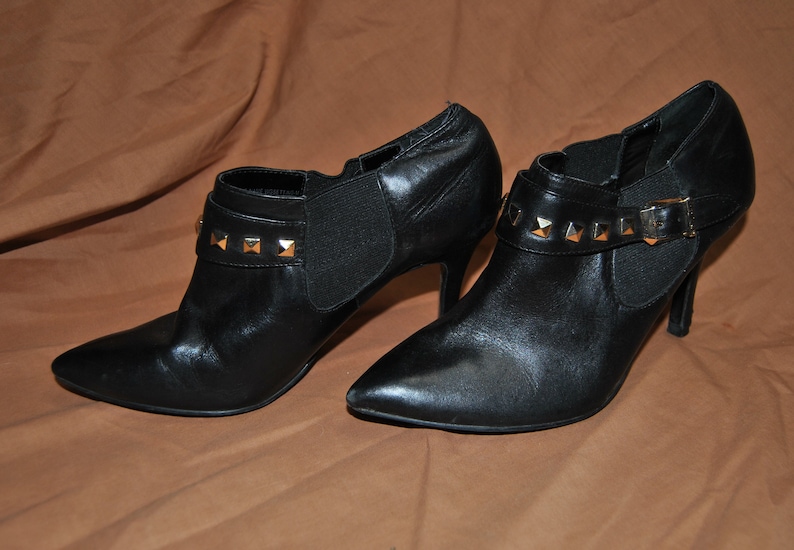 May include: A pair of black leather ankle boots with gold-toned studs and a pointed toe. The boots have a high heel and a back zipper closure.