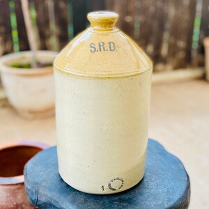 May include: A vintage ceramic jar with a yellow glaze and a white body. The jar has a wide mouth and a round body. The jar is labelled "S.R.D."