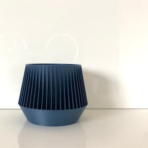 Peut inclure: Un pot en céramique bleu avec un design géométrique. Le pot a une base large et un sommet étroit, avec des lignes verticales qui descendent le long des côtés.