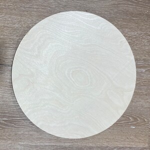 May include: A round, white wooden disc with a wood grain pattern. The disc is smooth and appears to be unfinished.