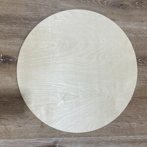 May include: A round, light wood circle with a smooth surface. The circle is on a wood background.