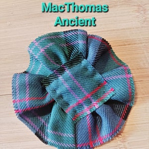 Könnte beinhalten: Eine grüne, blaue, rosa und rote karierte Stoffblume mit dem Text "MacThomas Ancient" darüber.
