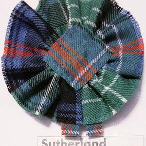 May include: A green, blue and red tartan fabric rosette with the text "Sutherland Old, Ancient" printed below.