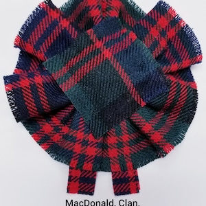 May include: A red, green, and blue tartan fabric rosette with frayed edges. The text "MacDonald, Clan, Modern" is printed below the rosette.