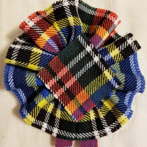 Puede incluir: Un lazo de corbata de tela a cuadros de colores con un borde rizado. El lazo de corbata está hecho de una tela tartán con rayas rojas, azules, amarillas, verdes y blancas.