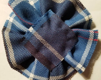 Può includere: Un fiore di tessuto a quadri blu, bianco e rosso con un bordo sfrangiato. Il tessuto è piegato e assemblato per creare una forma di fiore. Il testo "Navy, USA" è stampato sotto il fiore.