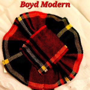 May include: A red, black, yellow and green tartan fabric circle with the text "Boyd Modern" above it.