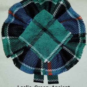 May include: A green, blue, and black tartan fabric rosette with the text "Leslie, Green, Ancient".