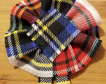 Può includere: Un fiocco in tessuto a quadri rossi, blu, bianchi, gialli e neri con bordi sfrangiati. Il fiocco è legato con un nodo in basso e il testo "Stewart Dress Modern" è stampato sotto il fiocco.