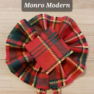 May include: Red, green, and yellow plaid fabric bow with frayed edges. The bow is made of a thick, woven fabric and has a square shape in the center.