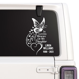 Op de afbeelding: Witte vinyl sticker met een vlinder, harten en de tekst "In Loving Memory Of My Daughter", een naam en data. Ontworpen voor toepassing op een voertuigruit.