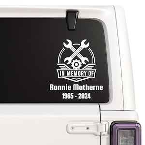 May include: A white vinyl decal applied to a vehicle window featuring a graphic of two crossed wrenches and a gear inside a circular emblem. Below the emblem, the text reads IN MEMORY OF, followed by the name Ronnie Matherne and the years 1965-2024.