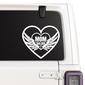 Könnte beinhalten: Weißer Aufkleber mit einem Herzdesign, dem Wort "MOM", den Jahren "1949-2025" und Engelsflügeln. Der Aufkleber ist für die Anbringung an einer Fahrzeugscheibe vorgesehen. Das Design ist schlicht und elegant.