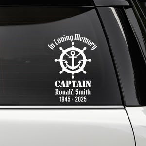 May include: White vinyl decal with the text "In Loving Memory" above a ship's wheel and anchor design. Below, it reads "CAPTAIN Ronald Smith 1945 - 2025". The decal is designed for application on a vehicle window.