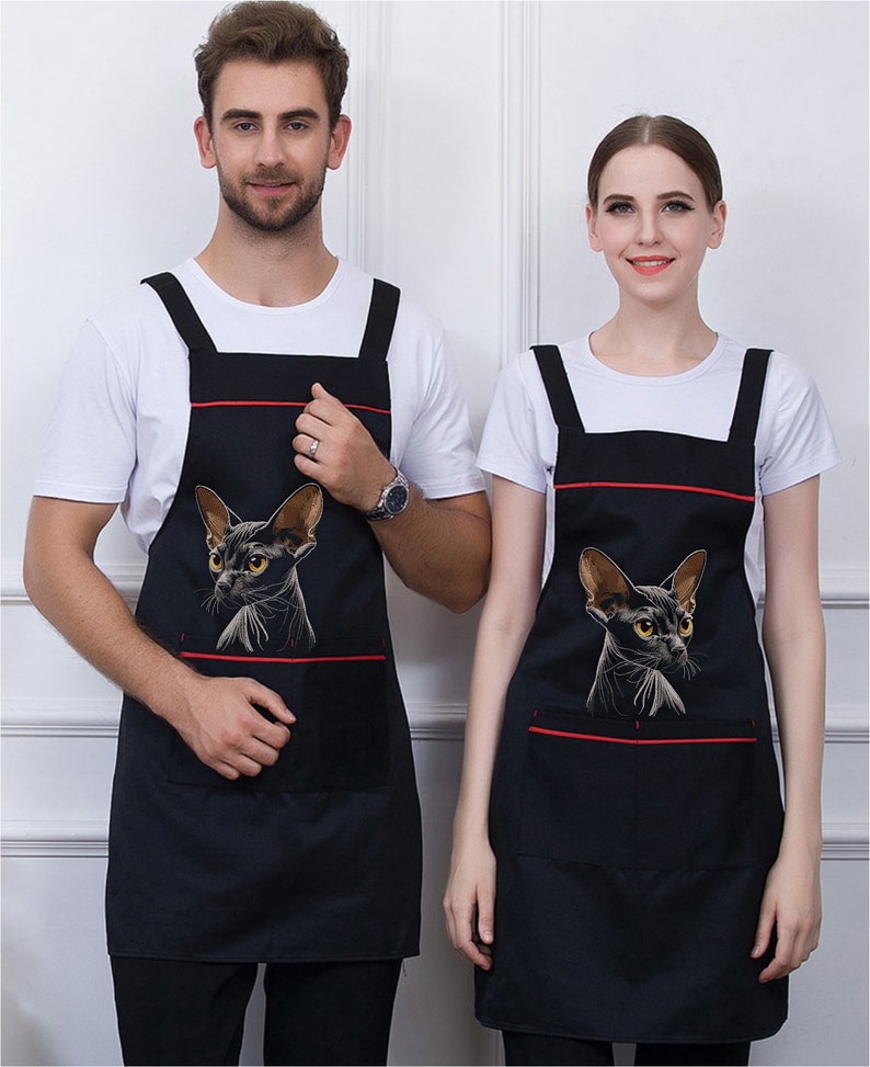 May include: Two black aprons with red trim and a black cat graphic. The aprons have a large pocket on the front.