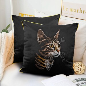 May include: Black pillow with yellow trim featuring an embroidered image of a tabby cat with green eyes. The cat is looking to the right and has a white patch on its chest.