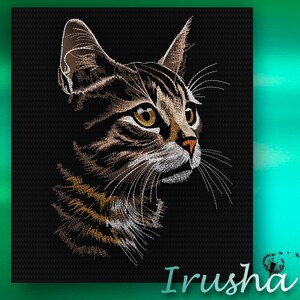 May include: A close-up of a brown tabby cat with white markings. The cat has green eyes and is looking to the right. The cat's fur is detailed with embroidery stitches.