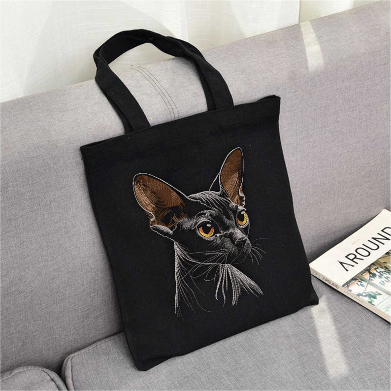 May include: Black canvas tote bag with an embroidered image of a black Sphynx cat with yellow eyes.