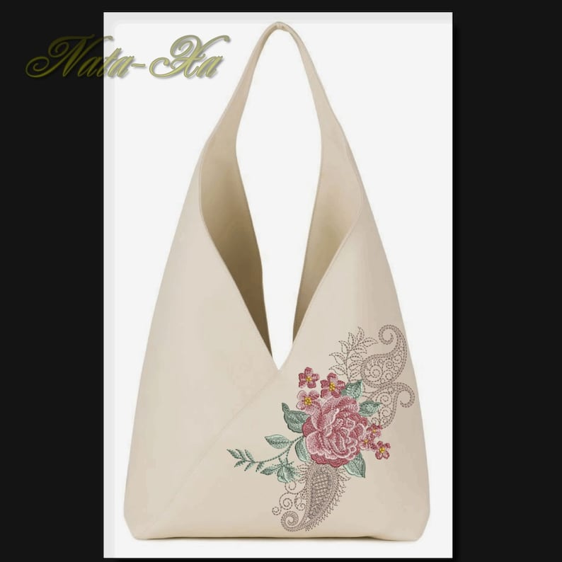 K&ouml;nnte beinhalten: Eine beige Canvas-Tragetasche mit einem floralen Stickmuster, das eine rosa Rose, gr&uuml;ne Bl&auml;tter und ein Paisley-Muster zeigt.