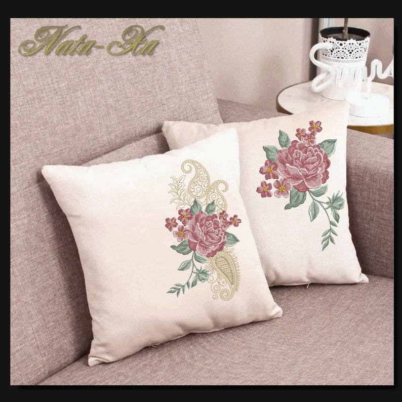 K&ouml;nnte beinhalten: Zwei wei&szlig;e Kissen mit gestickten Blumenmustern. Die Kissen zeigen rosa Rosen, gr&uuml;ne Bl&auml;tter und goldene Paisley-Muster.