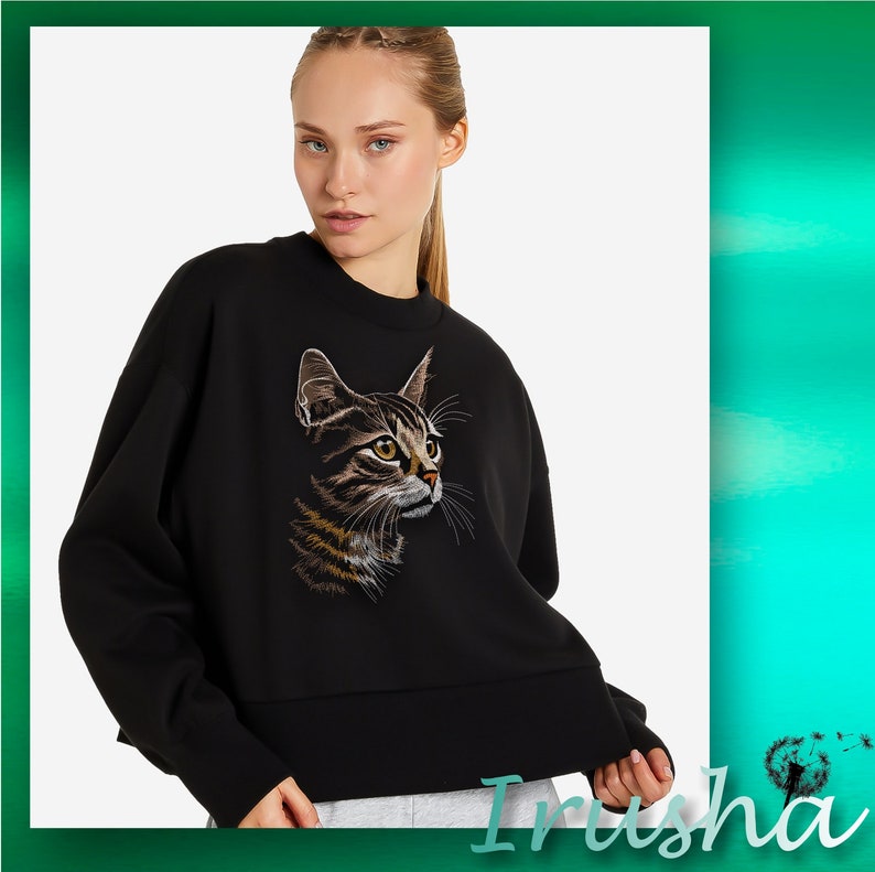 May include: Black sweatshirt with a brown and black cat embroidered on the front. The cat is looking to the right.