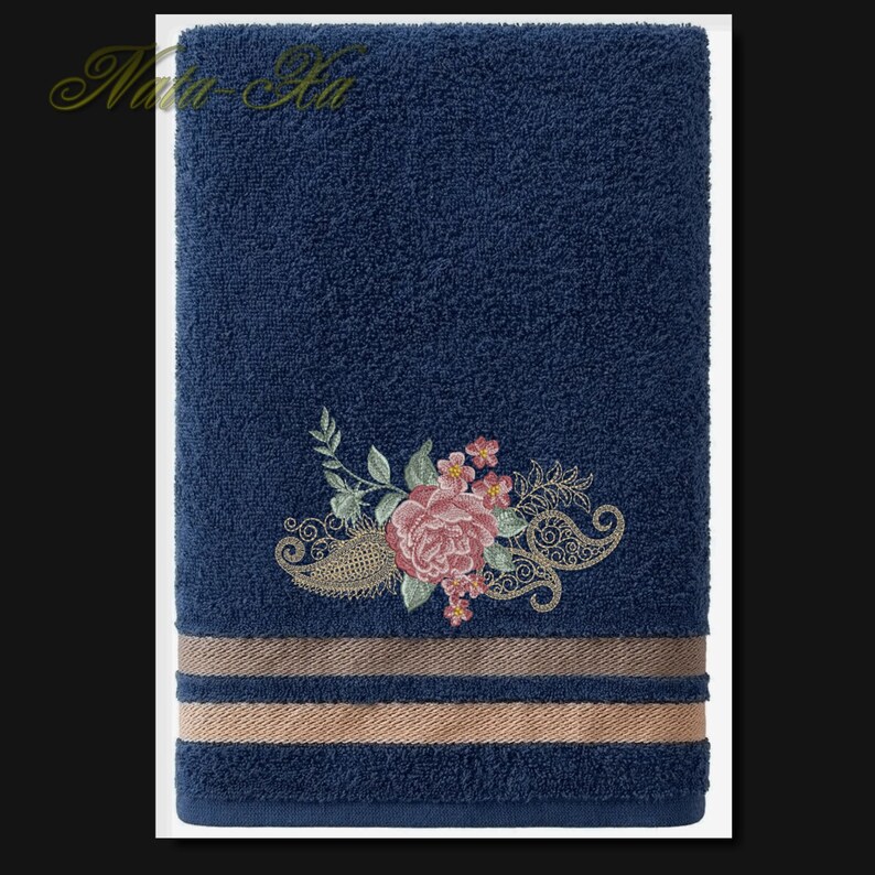K&ouml;nnte beinhalten: Ein dunkelblaues Badetuch mit einem floralen Stickmuster. Die Stickerei zeigt eine rosa Rose mit gr&uuml;nen Bl&auml;ttern und einem Paisley-Muster.