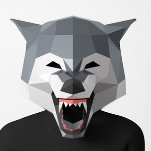 Op de afbeelding: Een grijs papieren wolfmasker met een grote open mond en scherpe tanden. Het masker is gemaakt van gevouwen papier en heeft een geometrisch ontwerp.