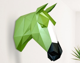 May include: A green papercraft horse head sculpture with a white face and black nose. The sculpture is mounted on a white wall.