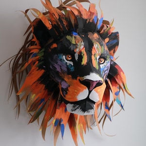 May include: A colorful paper mache lion head sculpture with a black face and orange mane. The sculpture is painted with various colors, including blue, green, and purple.