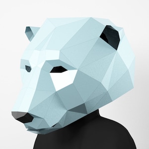 May include: A light blue papercraft polar bear mask. The mask is made of folded paper and has a geometric design. The mask is designed to be worn over the head.