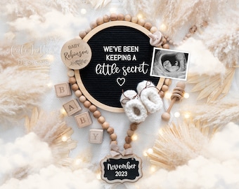 May include: A black letter board with the text "We've been keeping a little secret" and a heart.  The board is surrounded by wooden beads, a wooden baby block spelling "BABY", a wooden sign with the text "November 2023", a wooden sign with the text "Baby Robinson", a white knitted baby bootie, a wooden rattle, and a black and white ultrasound image.