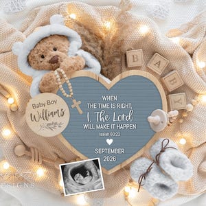 May include: A baby announcement with a teddy bear in a hooded outfit, wooden blocks spelling "BABY", and a heart-shaped sign with text. The sign reads "When the time is right, I, The Lord will make it happen" and "September 2026".